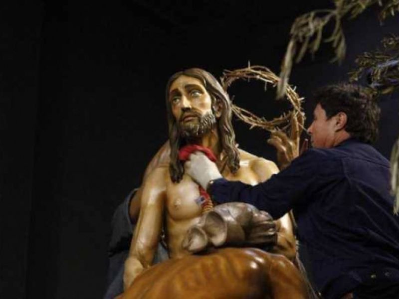 Trabajador realizando limpieza con un trapo en escultura de paso de Semana Santa