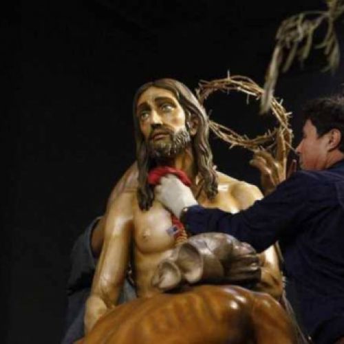 Trabajador realizando limpieza con un trapo en escultura de paso de Semana Santa